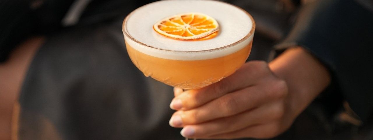 Elegante vrouw houdt cocktail met sinaasappel bij Secret Rooftop by Warwick in Brussel.