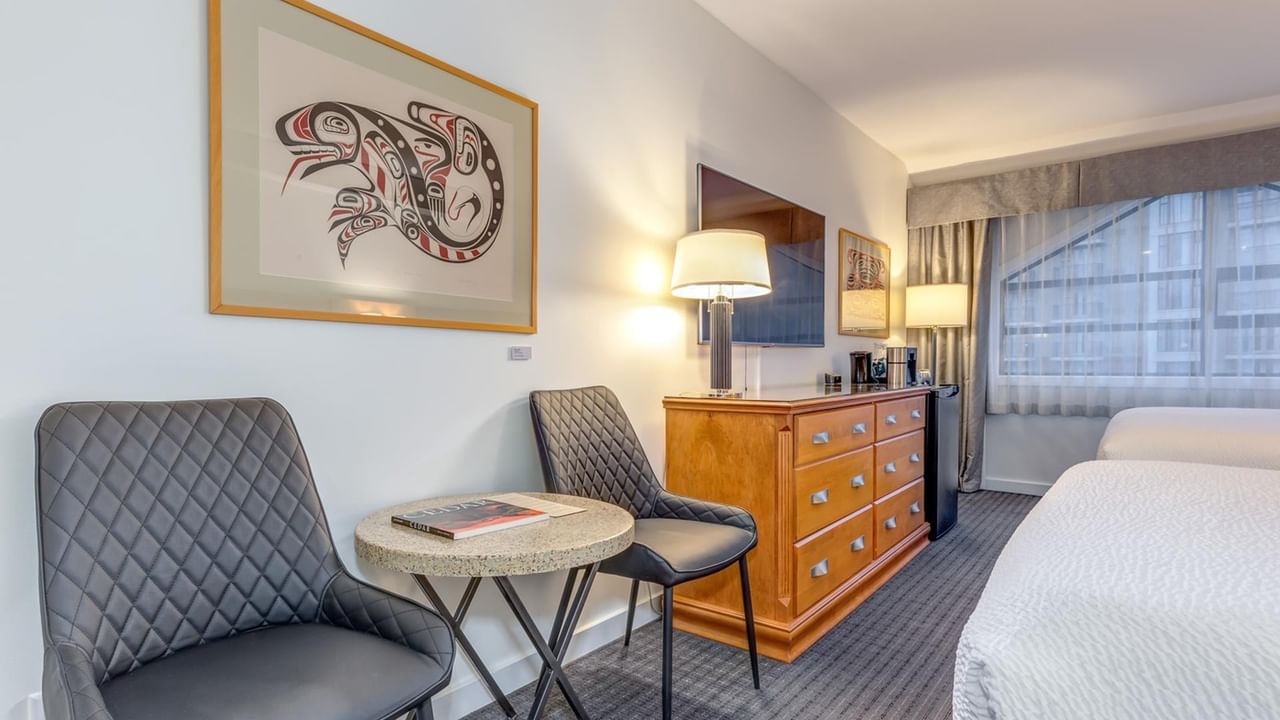 Hotel room with two beds, a dresser, a round table, two chairs, and a framed artwork.