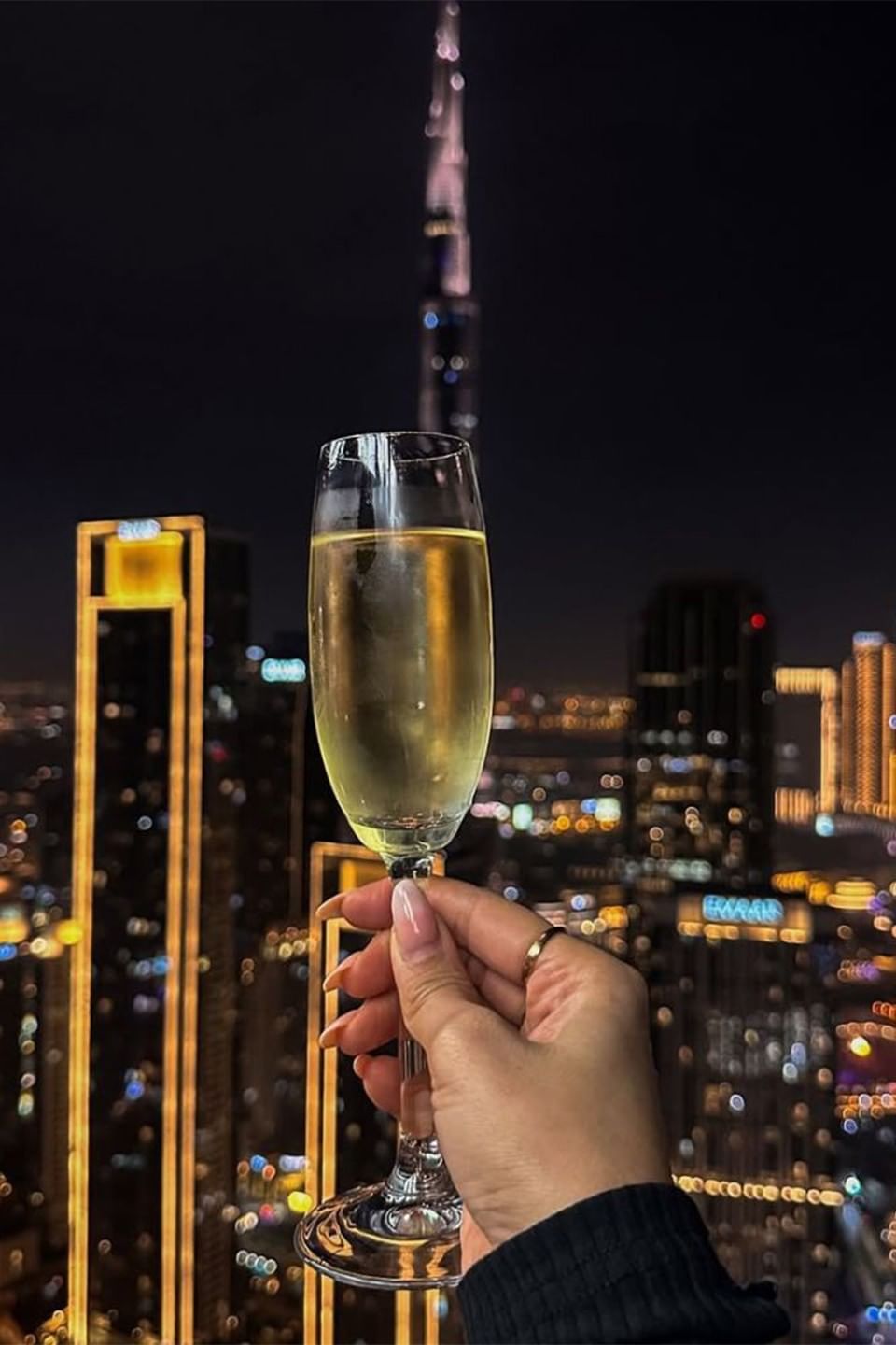 Hand holding a champagne flute against the glowing Dubai skyline at Malibu Sky Lounge & Bar with Burj Khalifa dining options