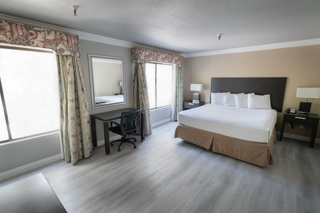 A wide-angle view of a hotel room with a king-sized bed, desk, and window.