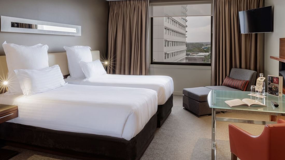 Two beds with a lounge chair by the window & carpet floors in the Superior Twin Single Room at Pullman Sydney Olympic Park