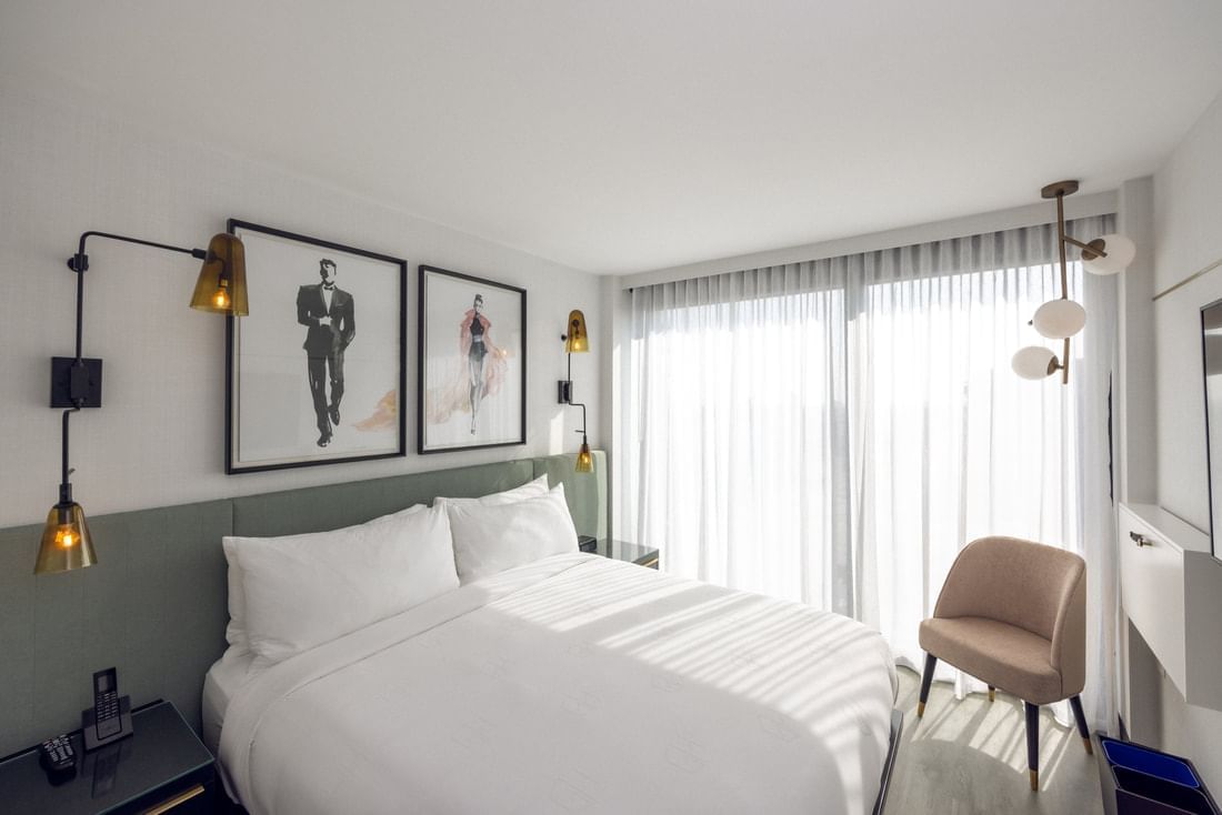 A hotel room with a king-sized bed, chair, and window