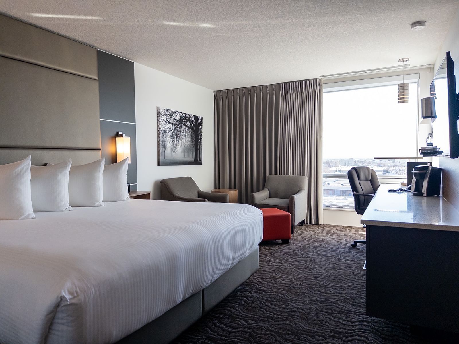 Premium 1 Queen room with king bed, seating area, and city view at Carriage House Hotel & Conference Centre, Calgary.