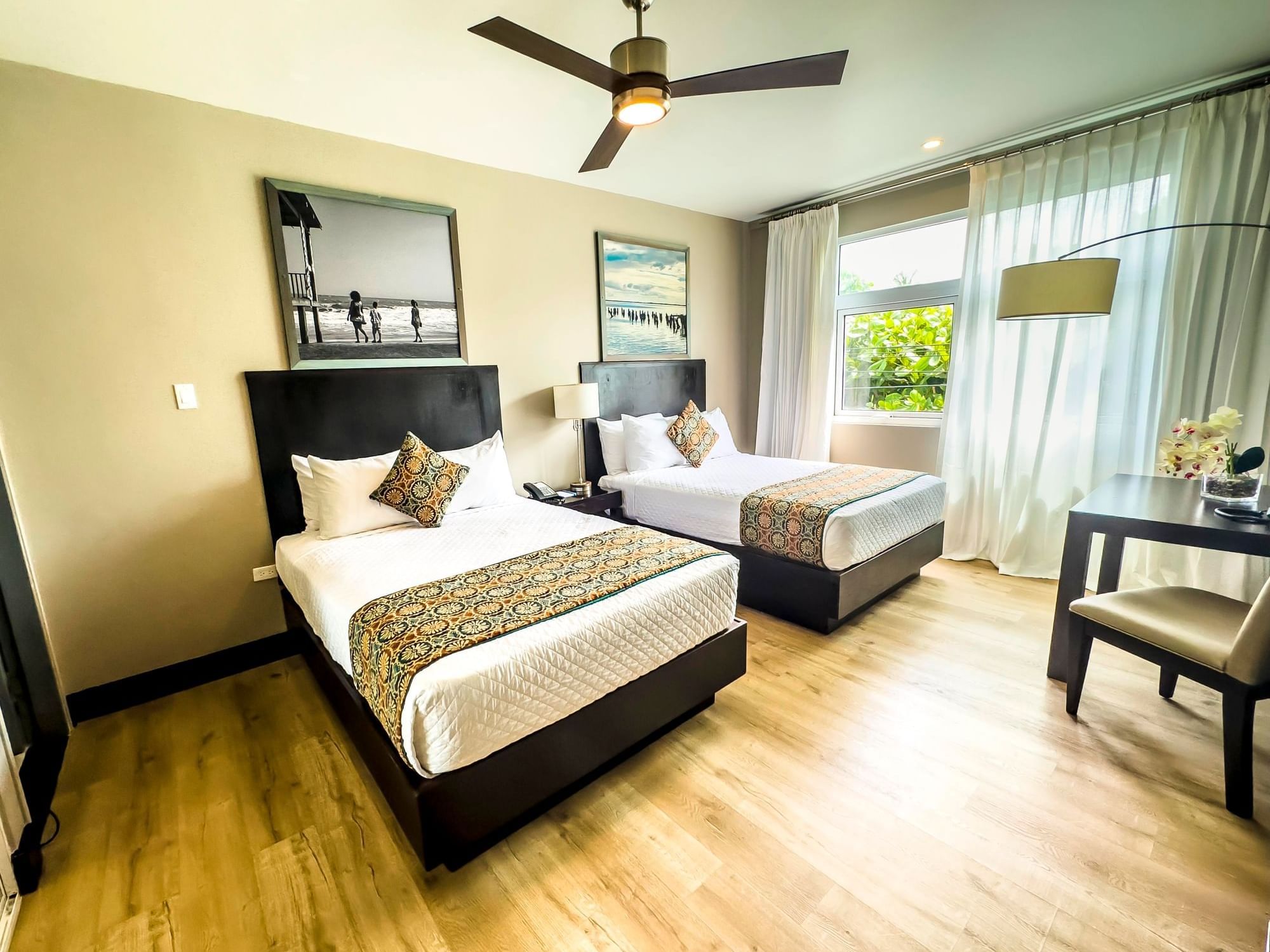 Bright room with two double beds, ceiling fan, large window with sheer curtains, and wood flooring at R Hotel Kingston.