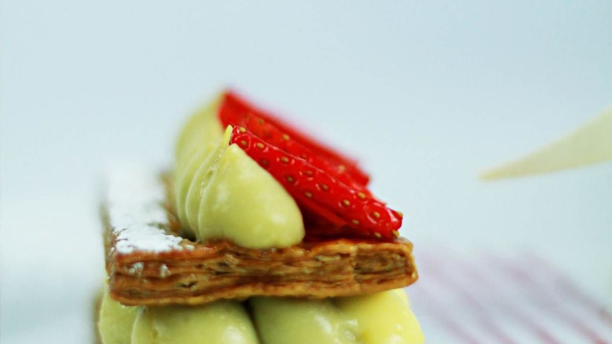 Assiette de gâteau en couches avec crème citron vert et fraises, décorée de lignes rouges et jaunes.