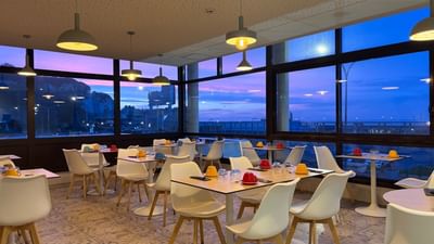 Panoramic view of a dining area with large windows and evening sky at L'Échappée Hôtel Casino Dieppe 4.