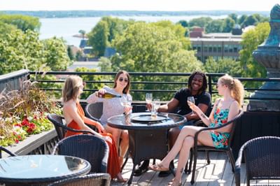 Friends cheering with wine glasses by a table on a rooftop deck under an open sky at Rodd Charlottetown Hotel