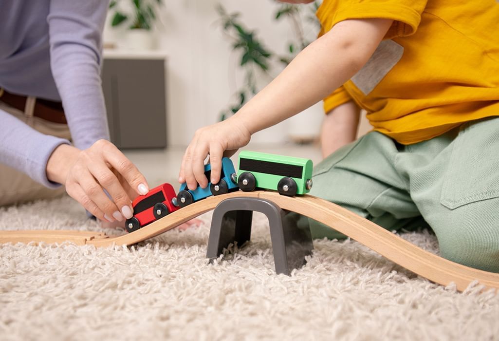 child and mother hands playing with wooden train set