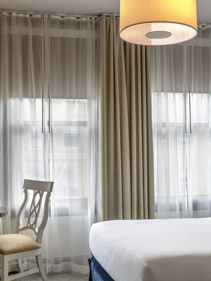 Round table by a white chair and tan curtains under a hanging lamp in Deluxe Queen Room at Warwick San Francisco