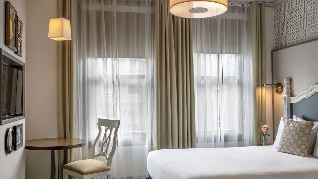 Round table by a white chair and tan curtains under a hanging lamp in Deluxe Queen Room at Warwick San Francisco