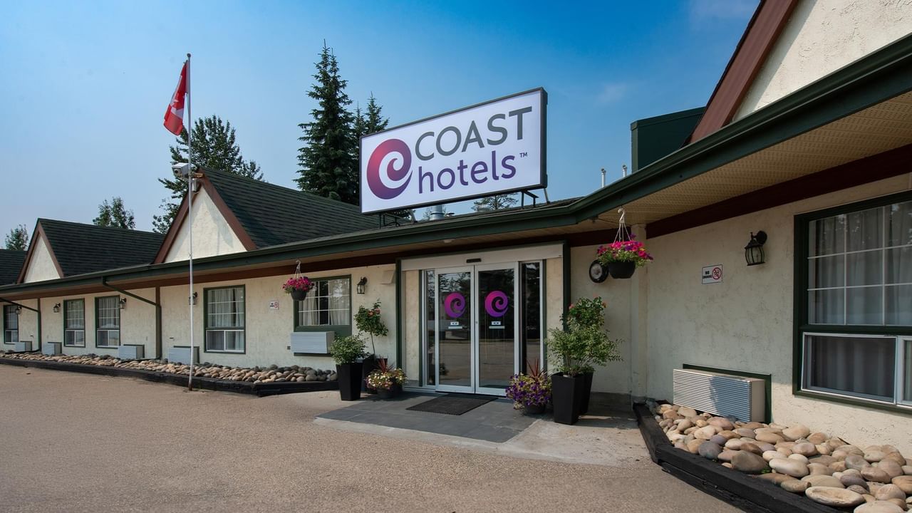 Exterior entrance of Coast Whitecourt Hotel property with trees and landscaping
