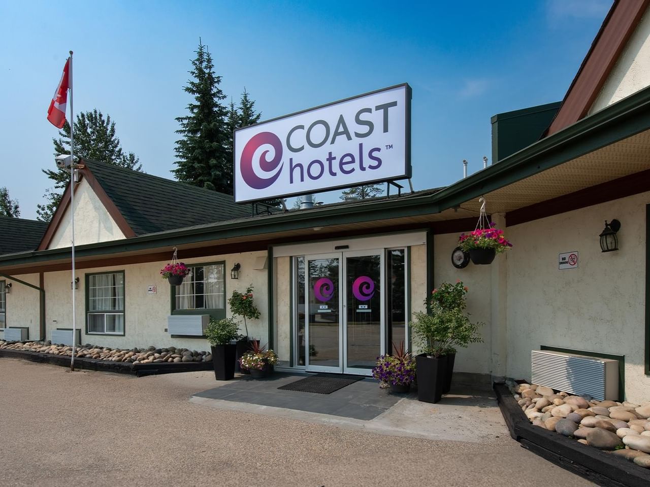 Exterior entrance of Coast Whitecourt Hotel property with trees and landscaping