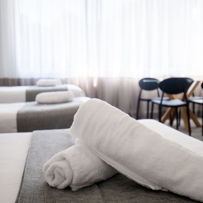 White towels on bed with two chairs and table in background at Mercure Charlestown.