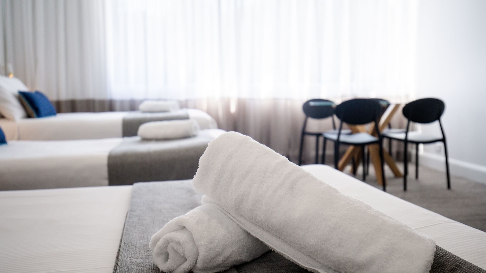 White towels on bed with two chairs and table in background at Mercure Charlestown.
