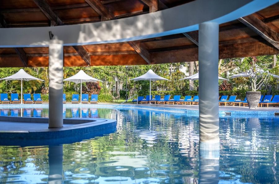 Blue lounge chairs by a sparkling pool under a wooden pavilion roof at The Naviti Resort - Fiji