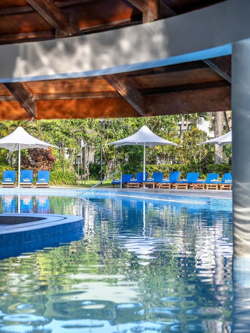 Blue lounge chairs by a sparkling pool under a wooden pavilion roof at The Naviti Resort - Fiji