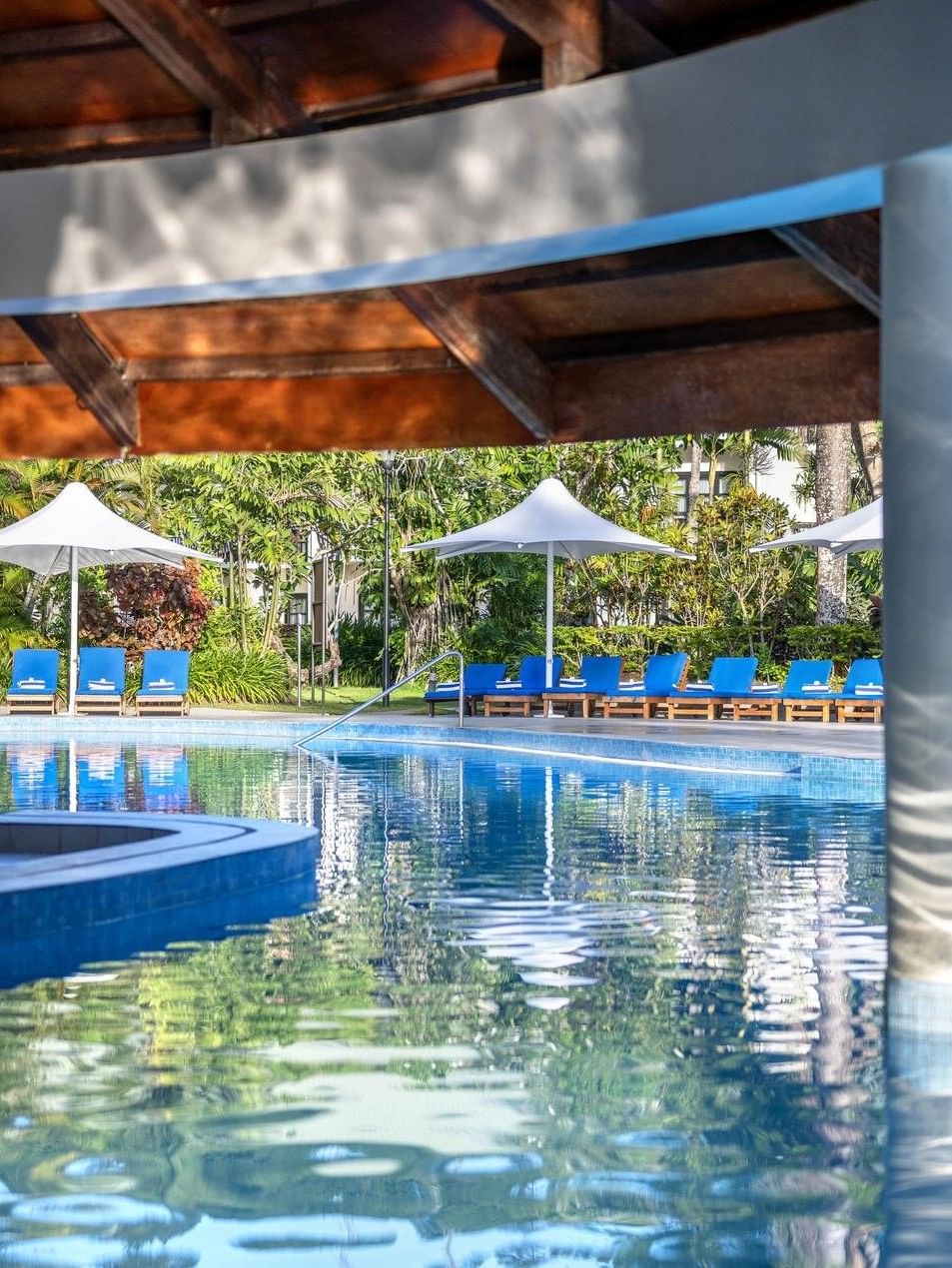 Blue lounge chairs by a sparkling pool under a wooden pavilion roof at The Naviti Resort - Fiji
