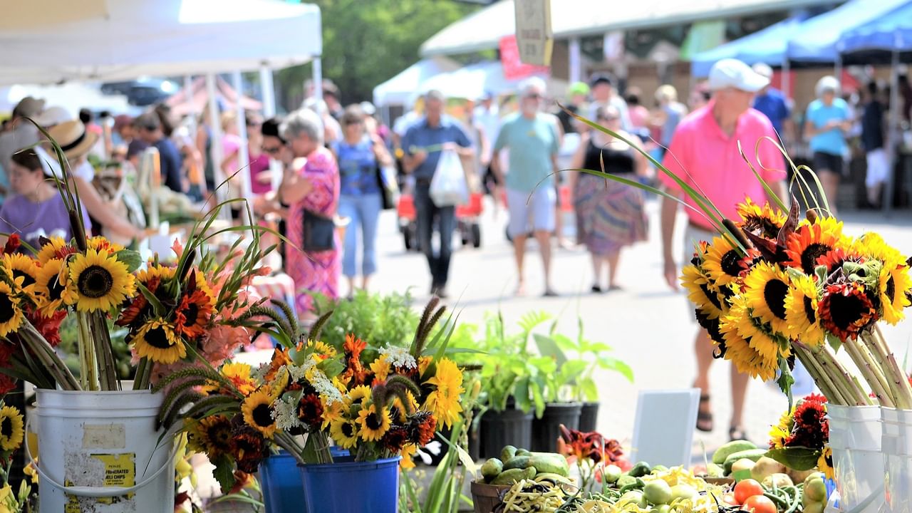 a bustling outdoor summer market with crowds browsing vendor tents and fresh produce