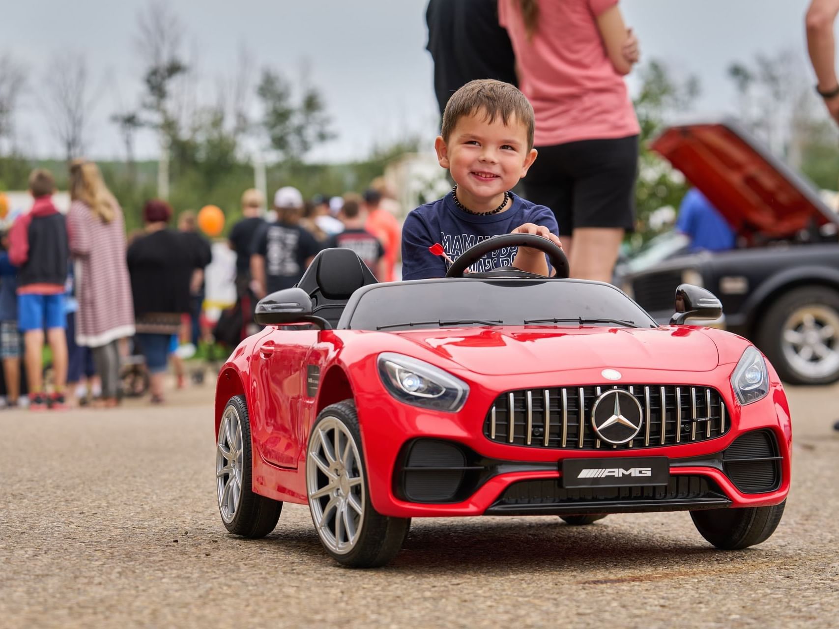 Small kid riding toy car by a gathering of people at Merit Hotel & Suites