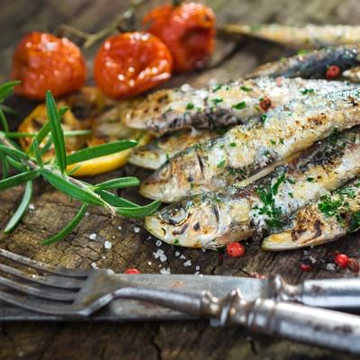 Geräucherte Fische, gewürzt mit Kräutern und Salz, liegen neben Tomaten auf einem rustikalen Holzbrett.
