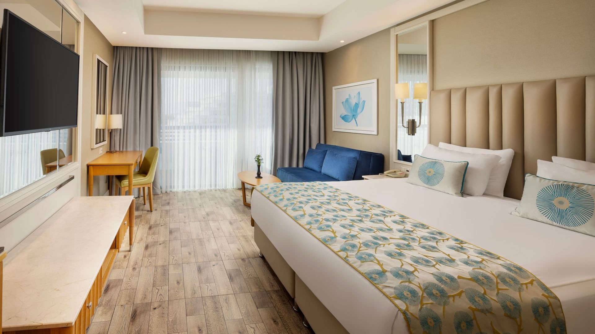 Colonel Suite with a large bed featuring blue floral bedding, a sofa, wooden flooring, and a desk at Titanic Deluxe Lara