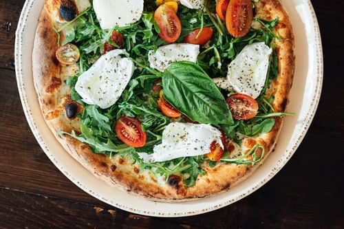 Fresh arugula pizza with burrata and sliced tomatoes on a white ceramic plate at Warwick Denver