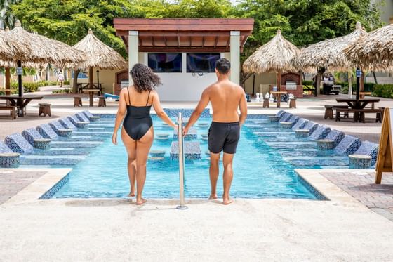 A couple holding hands & standing at the edge of the pool