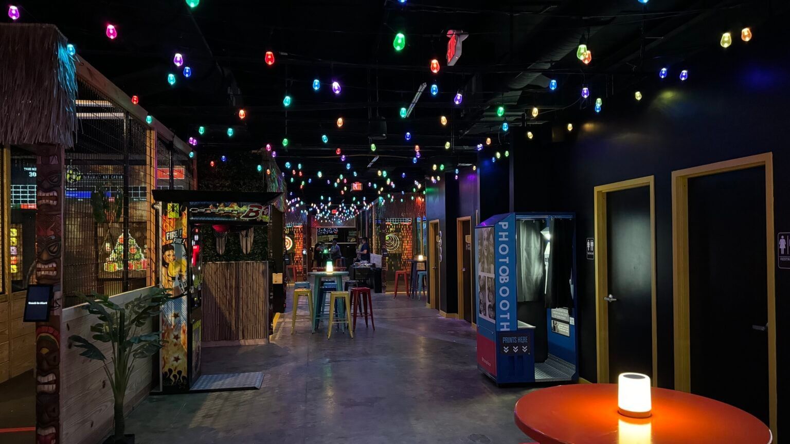 A dark interior with lots of colorful chairs and hanging overhead lights at Bananas' Axe Cabana.
