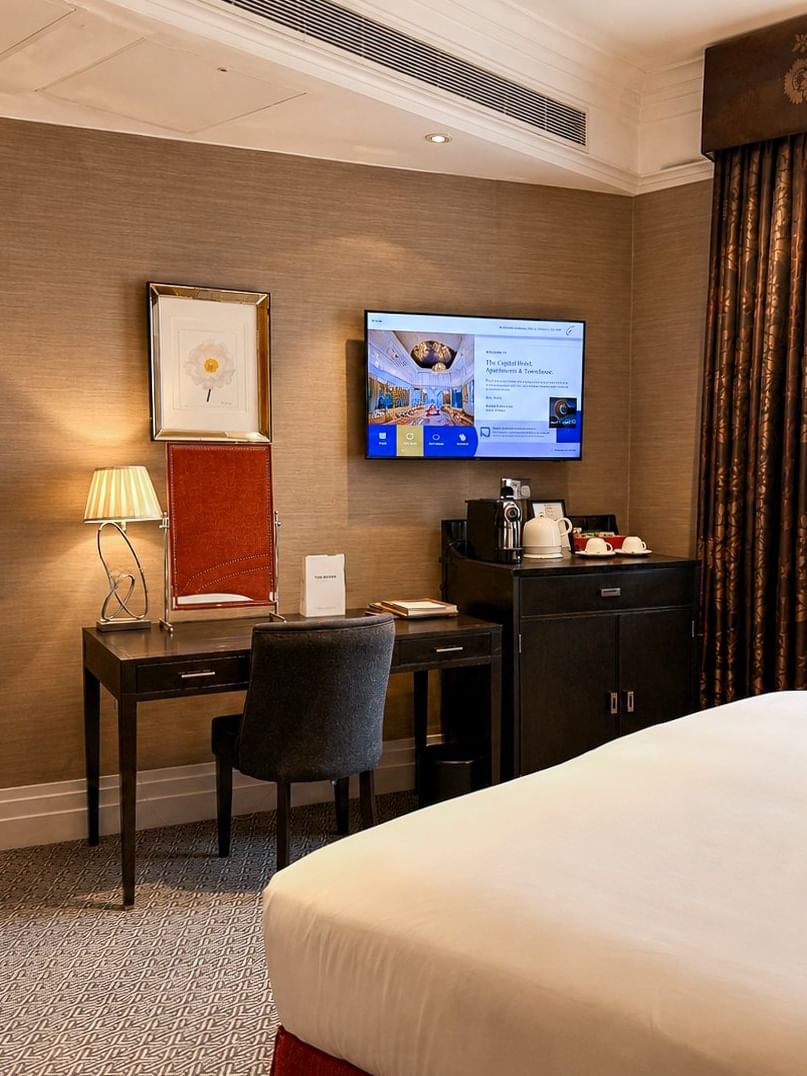 Wooden desk by a dark chair under a wall-mounted TV surrounding a large wardrobe at Warwick Hotels & Resorts