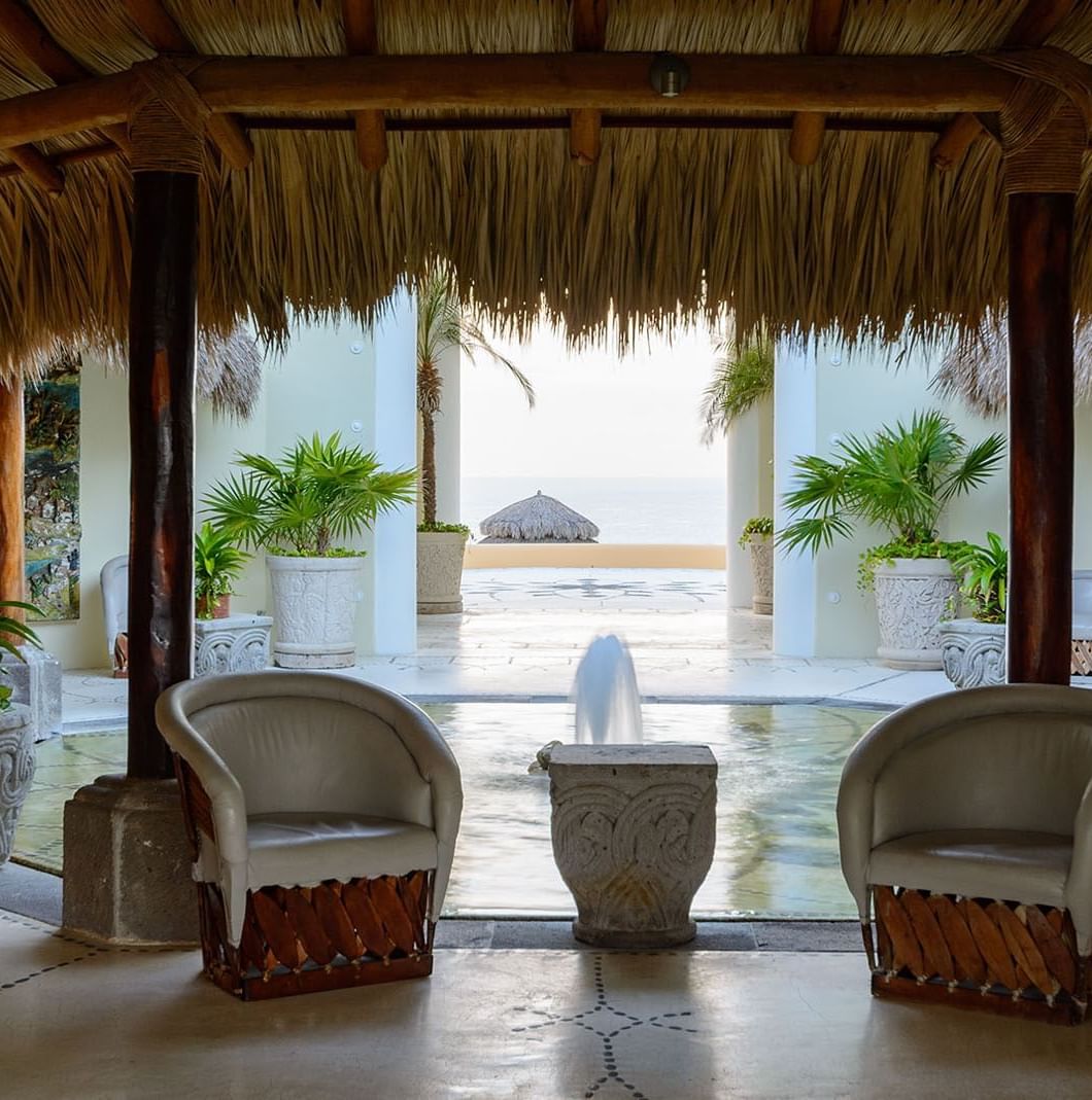 Lobby area featuring two white armchairs, a small fountain, and potted plants at Quinta Real Huatulco