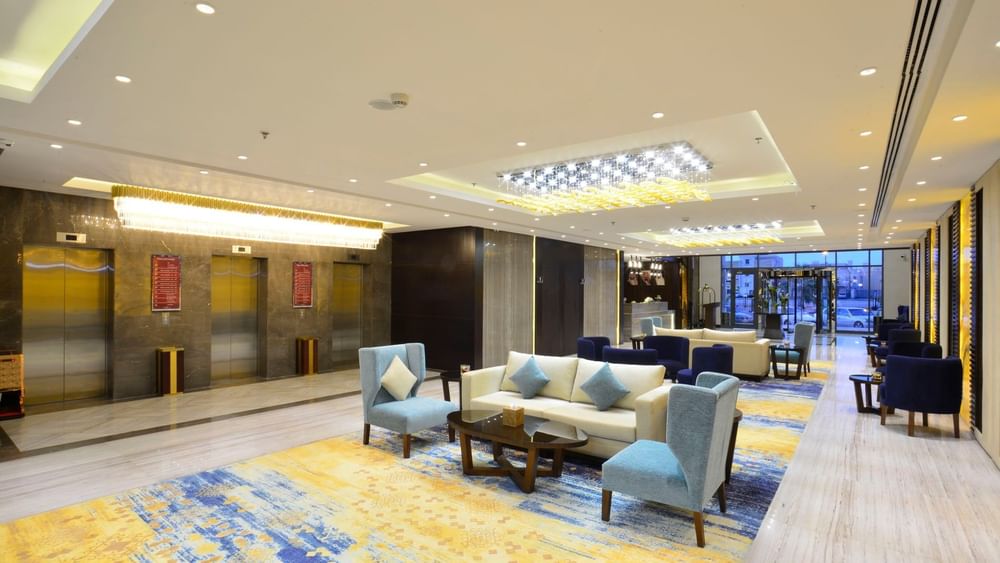 Hall d'ascenseur, avec des fauteuils bleu clair près d'un canapé crème, sous des lustres, au Naviti By Warwick Dammam