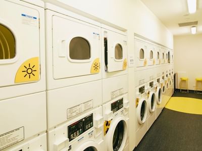 Row of white washers and dryers in a clean, bright laundry room at La Trobe University Menzies College.