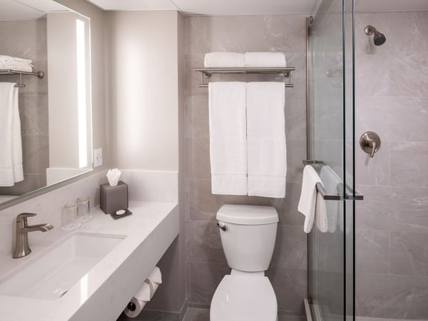 Modern bathroom with white sink, toilet, towels, and glass shower stall with a handheld showerhead.