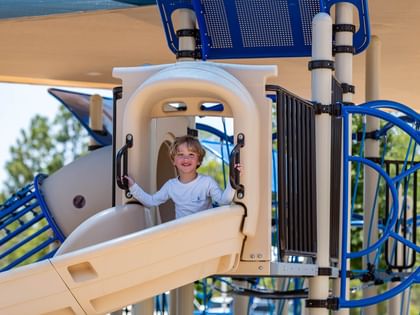 Child smiling on blue and beige playground structure at Camp Creek Inn in Inlet Beach