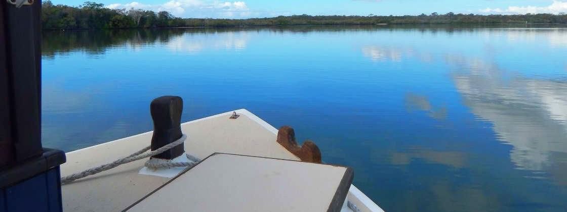 Calm waterway reflects the sky and clouds as seen from the bow of a boat near the Novotel Sunshine Coast Resort