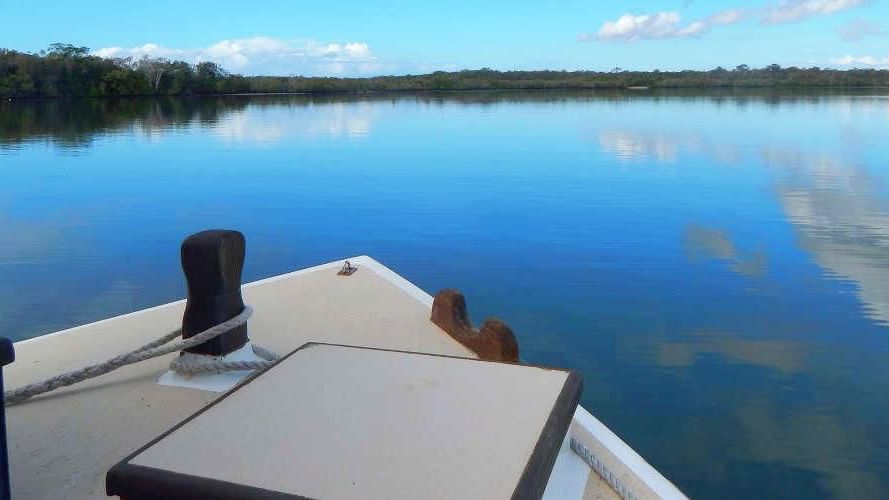 Calm waterway reflects the sky and clouds as seen from the bow of a boat near the Novotel Sunshine Coast Resort