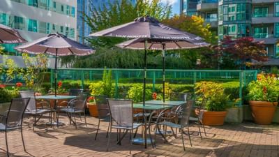 Outdoor patio with tables, umbrellas, and lush plants at Rosedale on Robson Suite Hotel near cruise port in Vancouver, BC