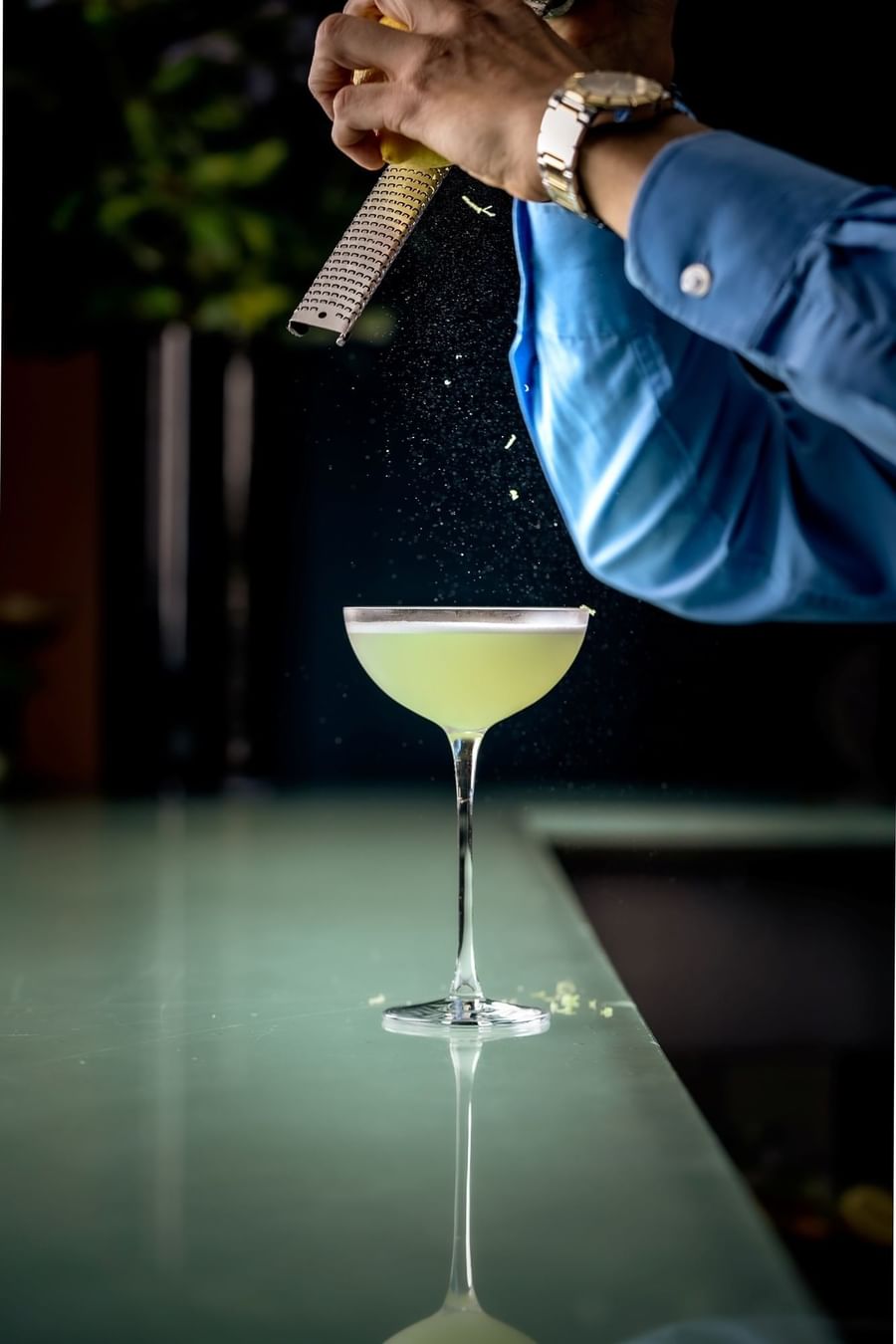 Bartender zesting citrus peel over green cocktail in coupe glass on counter at Tom Brown at The Capital