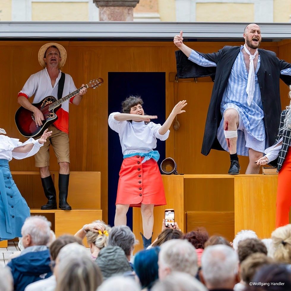 Performers in casual costumes on stage with audience watching an event.