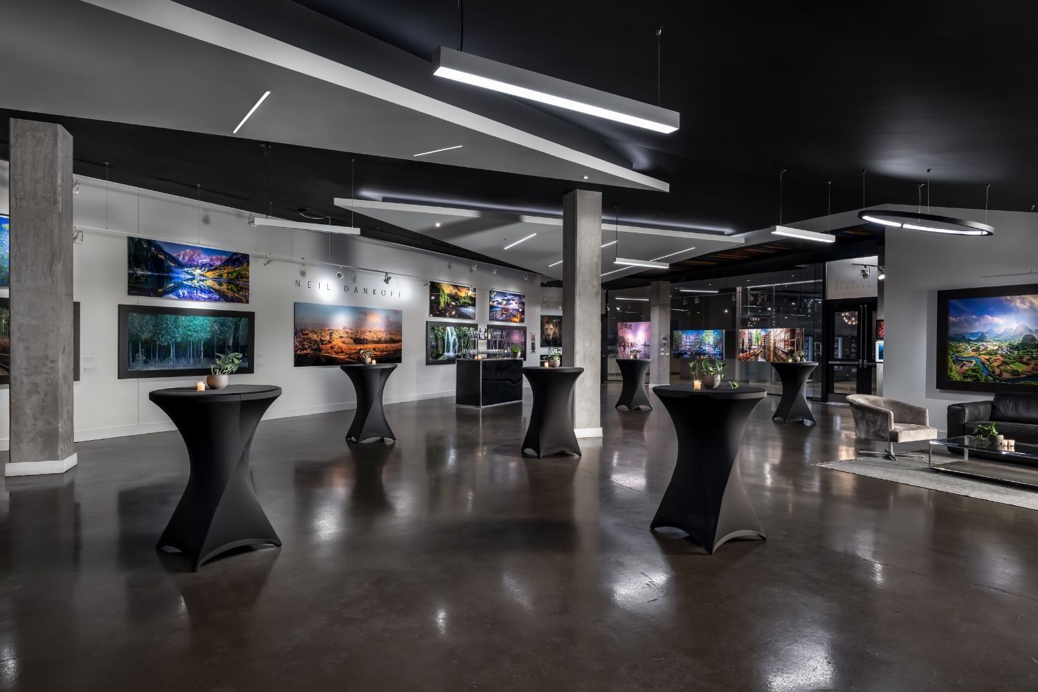 Cocktail tables with black covers set up near framed landscape photographs in an art gallery space at Hotel X Toronto