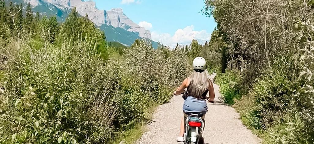 Woman biking on a forested trail with mountain views near Canmore.