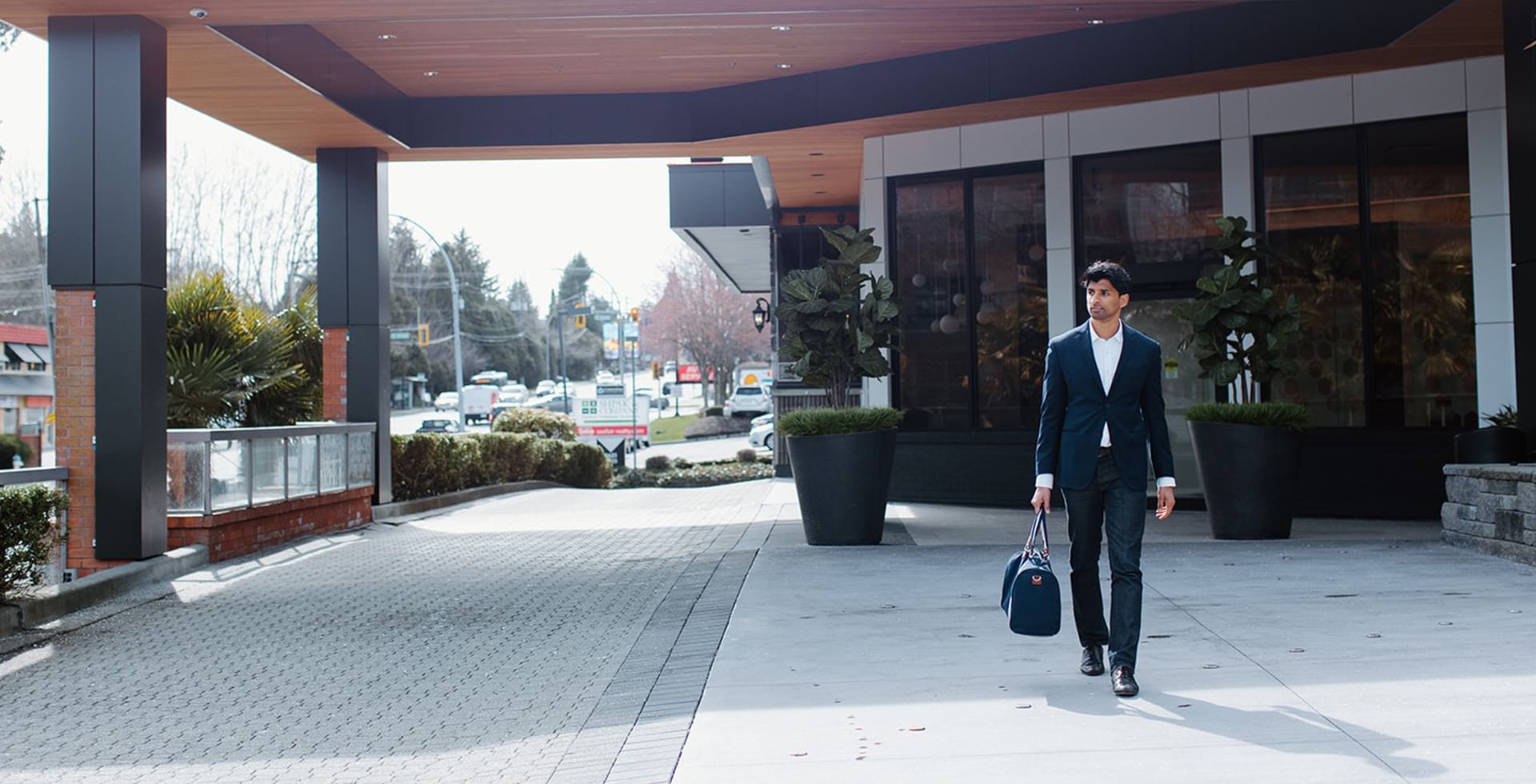 man in suite walking with a bag in hand in front of Coast Tsawwassen Inn