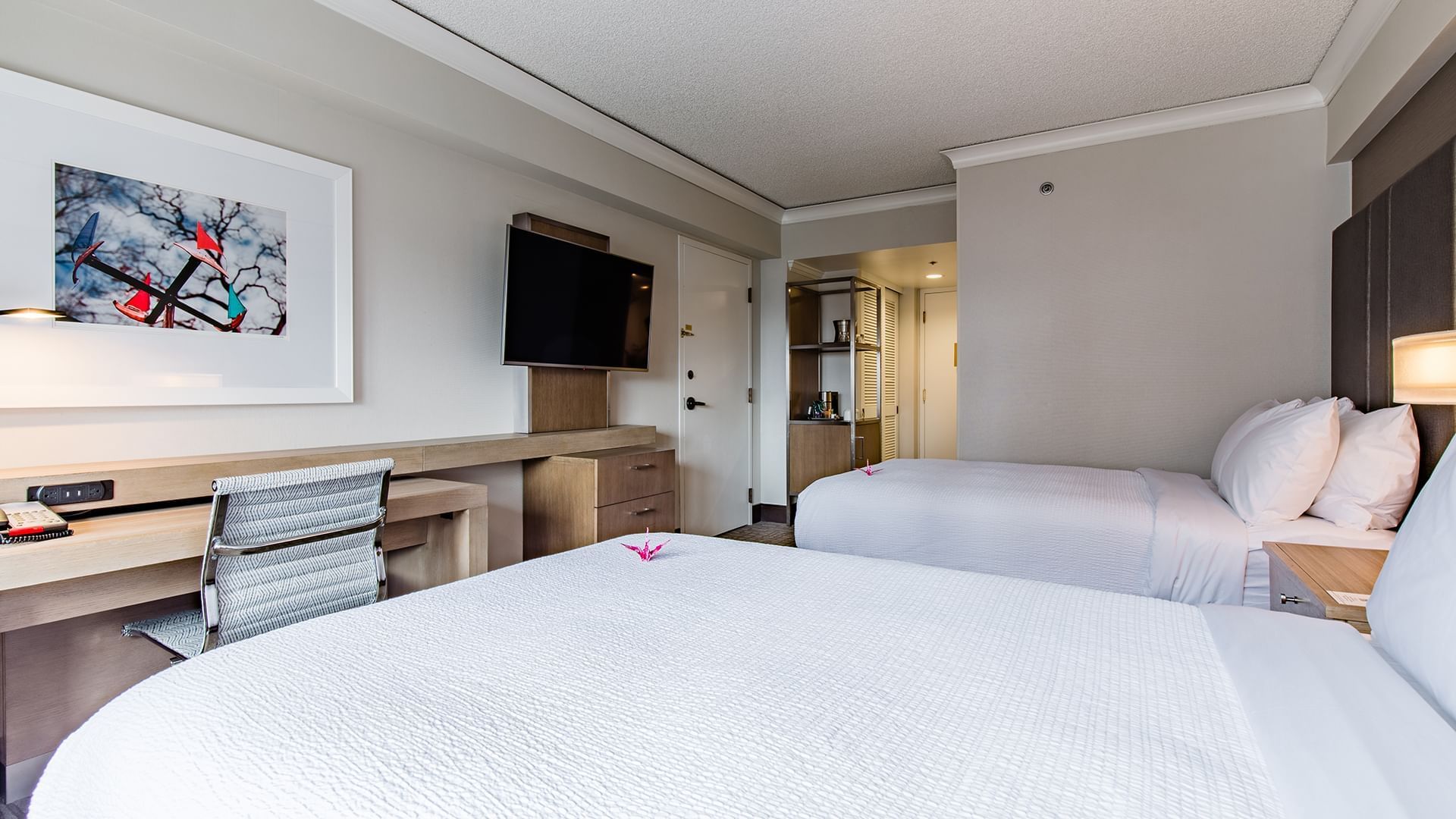 A hotel room with two double beds, a desk, and a TV on the wall.