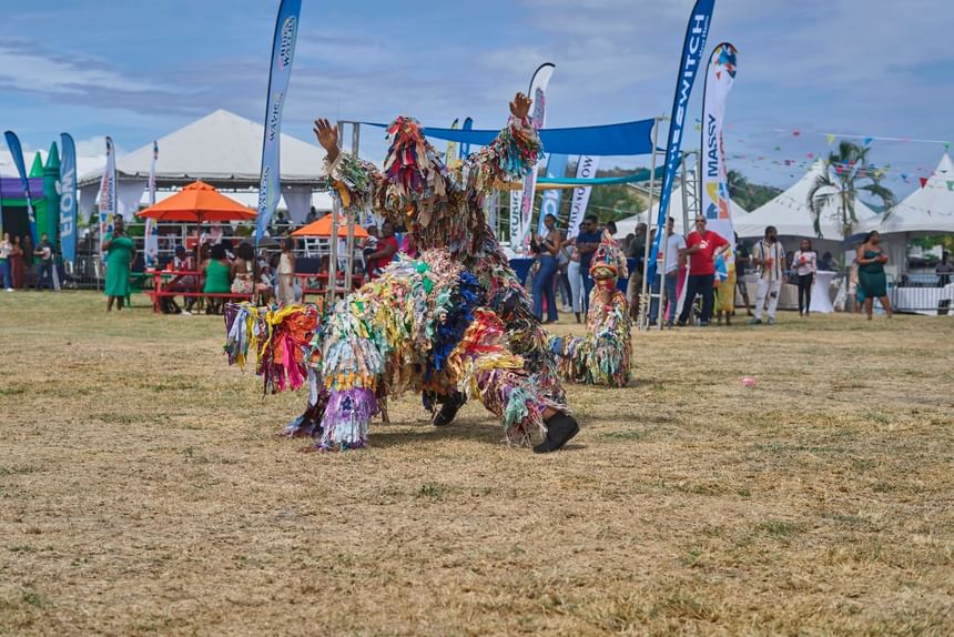 Performer in colorful ragged costume dances energetically at Taste The Bay 2025 festival near Bay Gardens Hotels and Resorts
