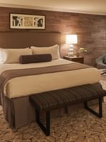 Large bed by a grey chair under framed art on a wood wall in Premier Junior Suites at Warwick Denver