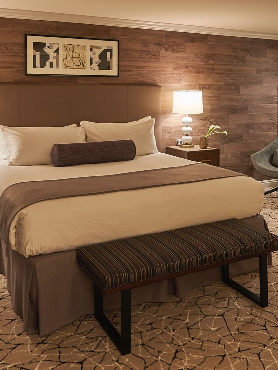 Large bed by a grey chair under framed art on a wood wall in Premier Junior Suites at Warwick Denver