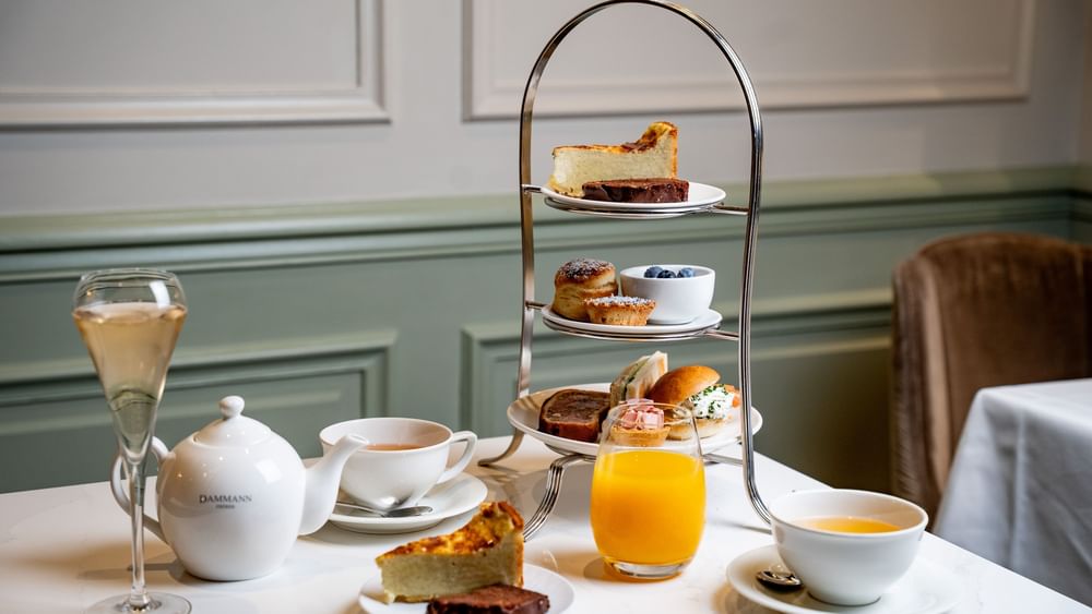 Tiered stand of snacks and pastries served with juice by a teapot on a white marble table at Hotel Westminster Paris