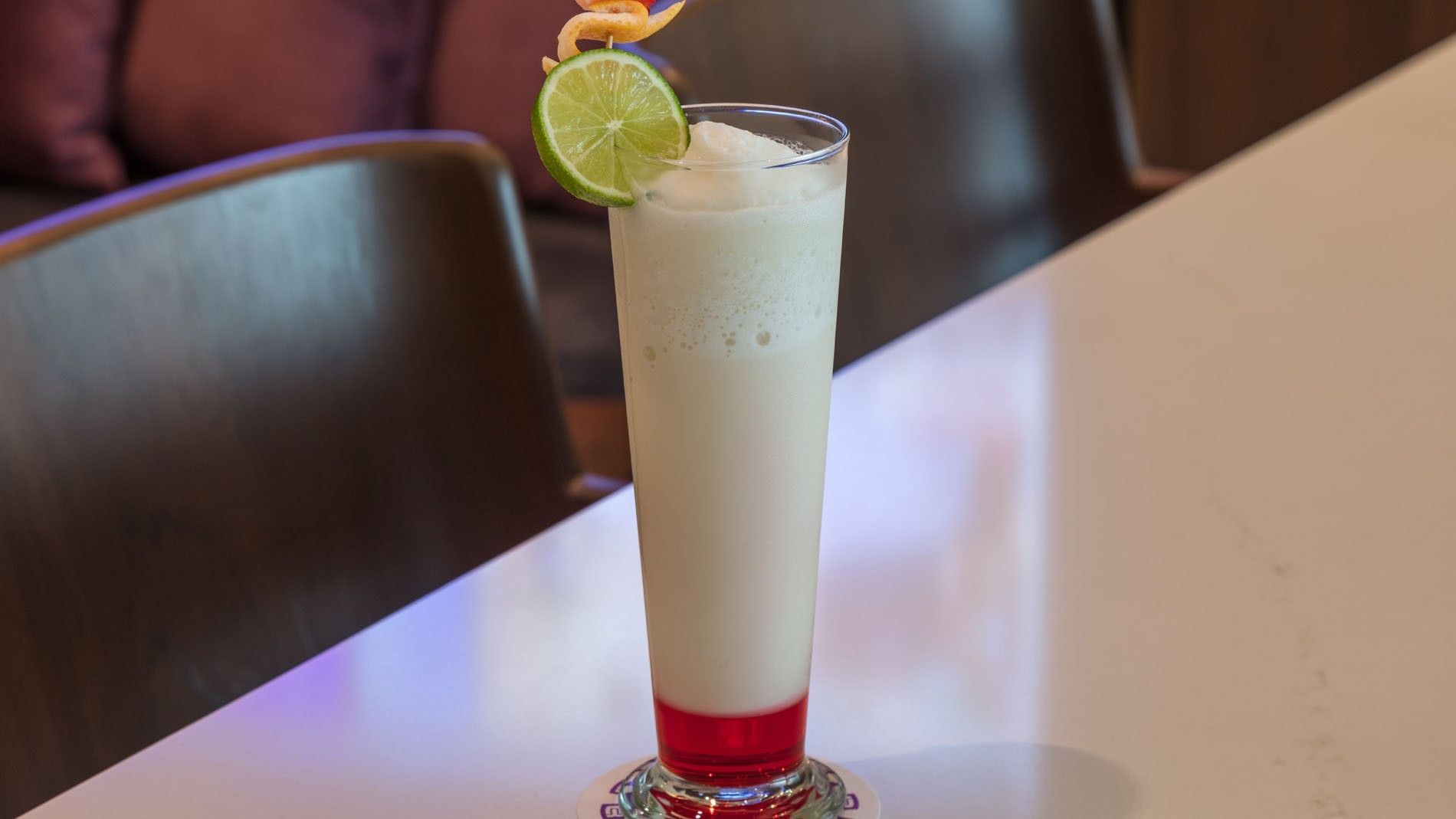 Creamy cocktail served in a tall glass with a lime garnish on a sleek white table in Lobby Bar at Camino Real Merida
