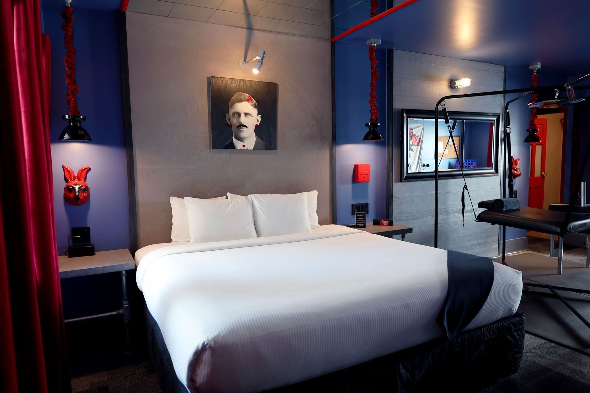 A neatly made bed with white linens and pillows against a gray wall with a portrait of a man.
