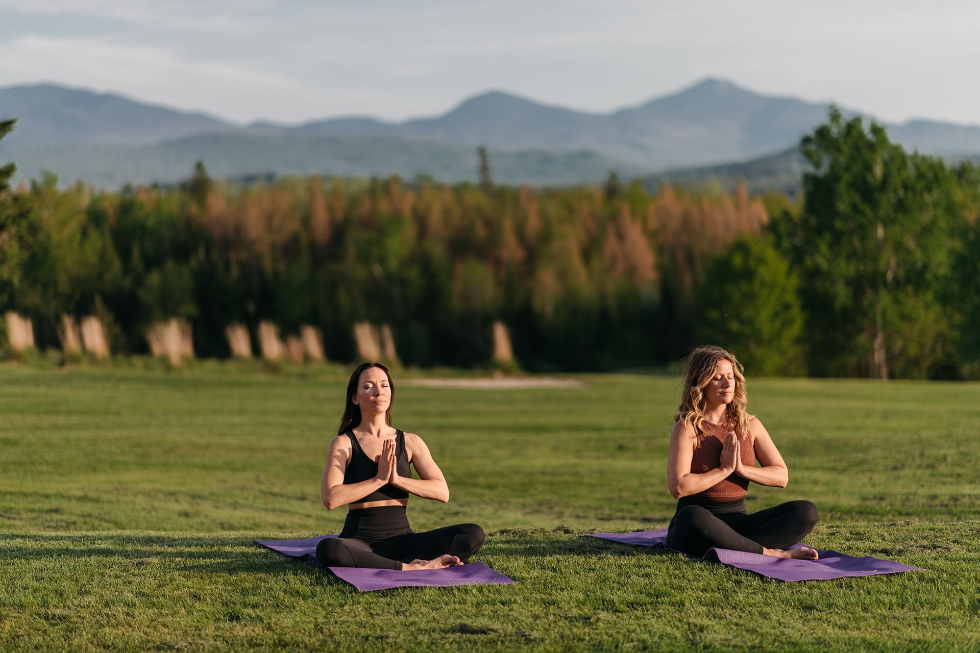 Two women doing yoga on mats on green grass with mountain views at Mountain View Grand Resort & Spa
